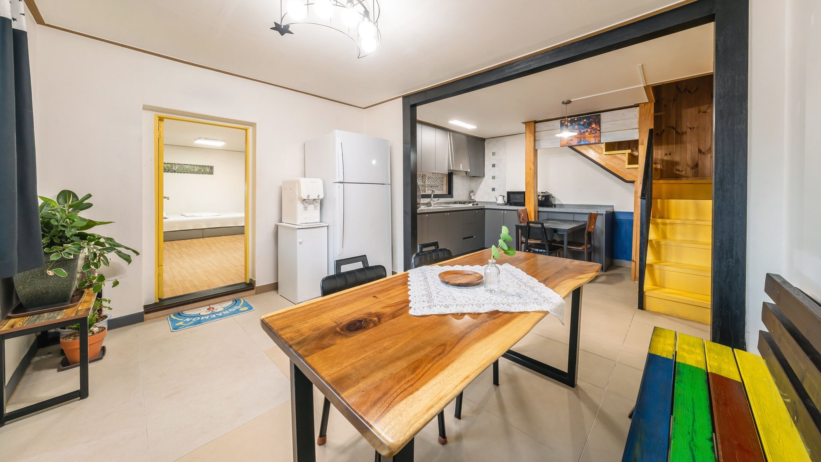 Eine moderne Küche mit weißen Geräten, ein Essbereich mit einem Holztisch und eine Treppe, die zu einer oberen Ebene führt.
