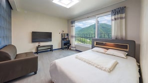 Habitación de hotel con una cama grande, televisión, escritorio, silla y ventana con vista a la montaña.
