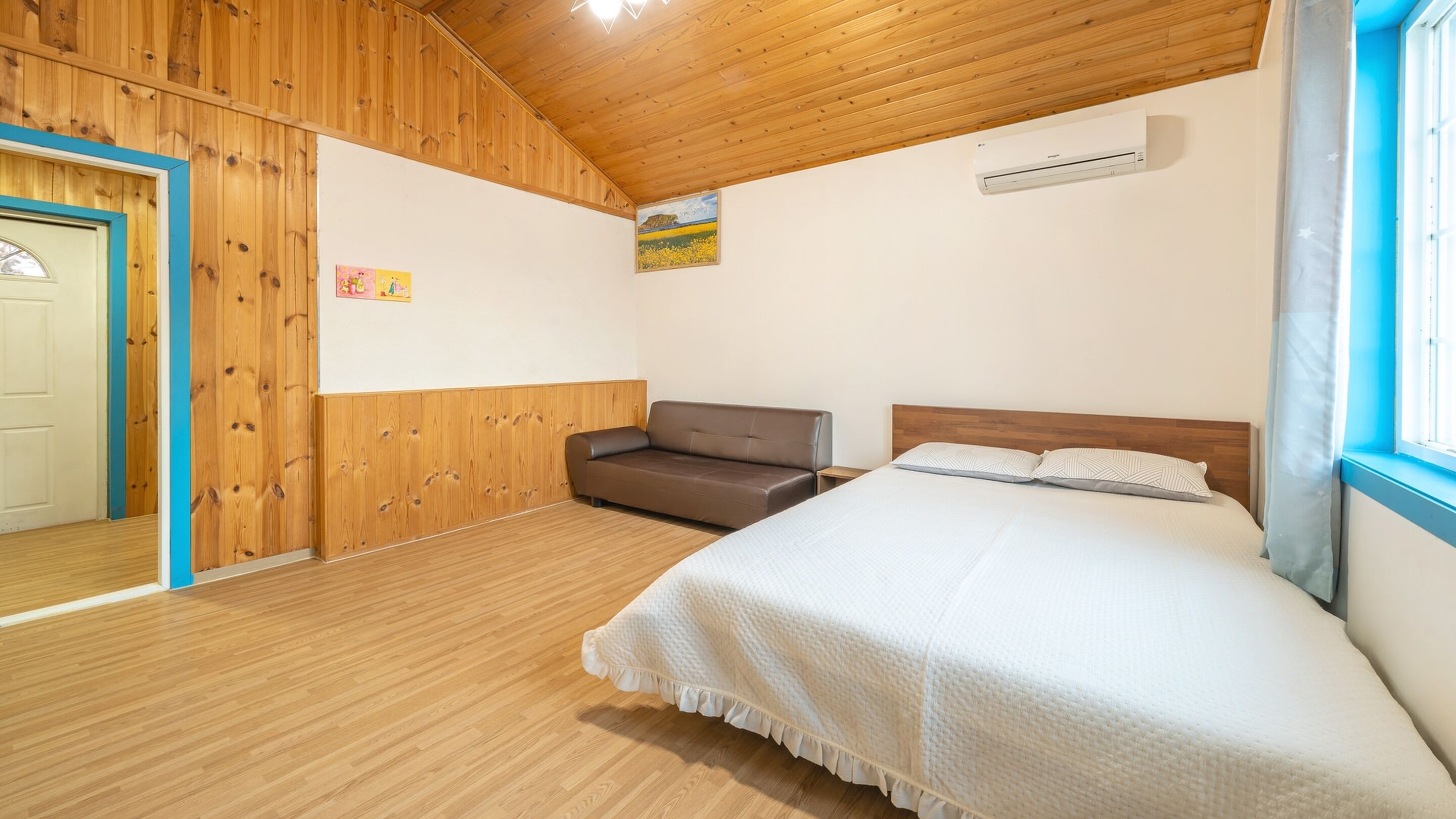A bedroom with a wooden ceiling, a bed with white bedding, a brown sofa, and a painting on the wall.