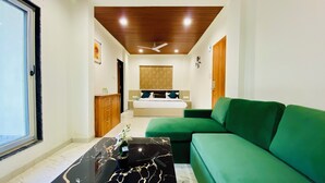 A hotel room with a bed, a green sofa, a marble coffee table, and a ceiling fan. - Stay 10 Parallel Apartment Hotel (Indore)