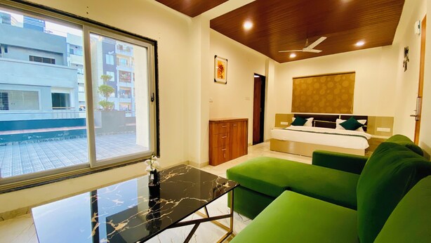 A modern hotel room with a large window, a bed with green bedding, a green sofa, a marble table, and a ceiling fan. - Stay 10 Parallel Apartment Hotel (Indore)