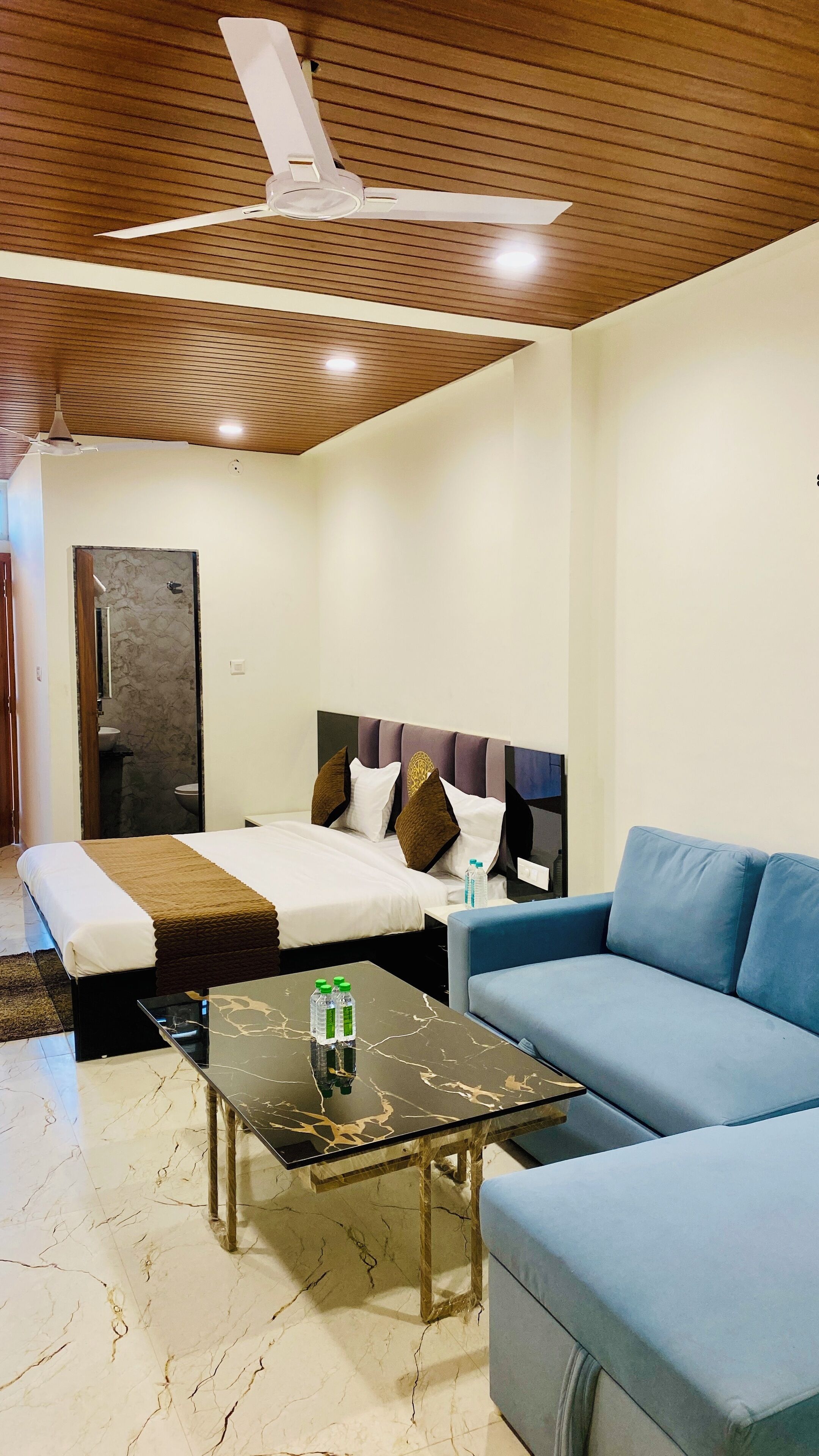 A hotel room with a bed, a sofa, a table, and a ceiling fan.