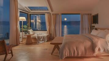 Un dormitorio con una cama grande, una mesita de noche, una silla y un ventanal con vistas al agua.