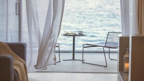 Una habitación con vistas al mar, una mesa con un libro y una taza, y una silla.