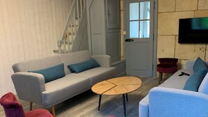 A modern living room with a grey sofa, two armchairs, a coffee table, and a TV mounted on a stone wall. - Family country house for 11 people (Bulson)