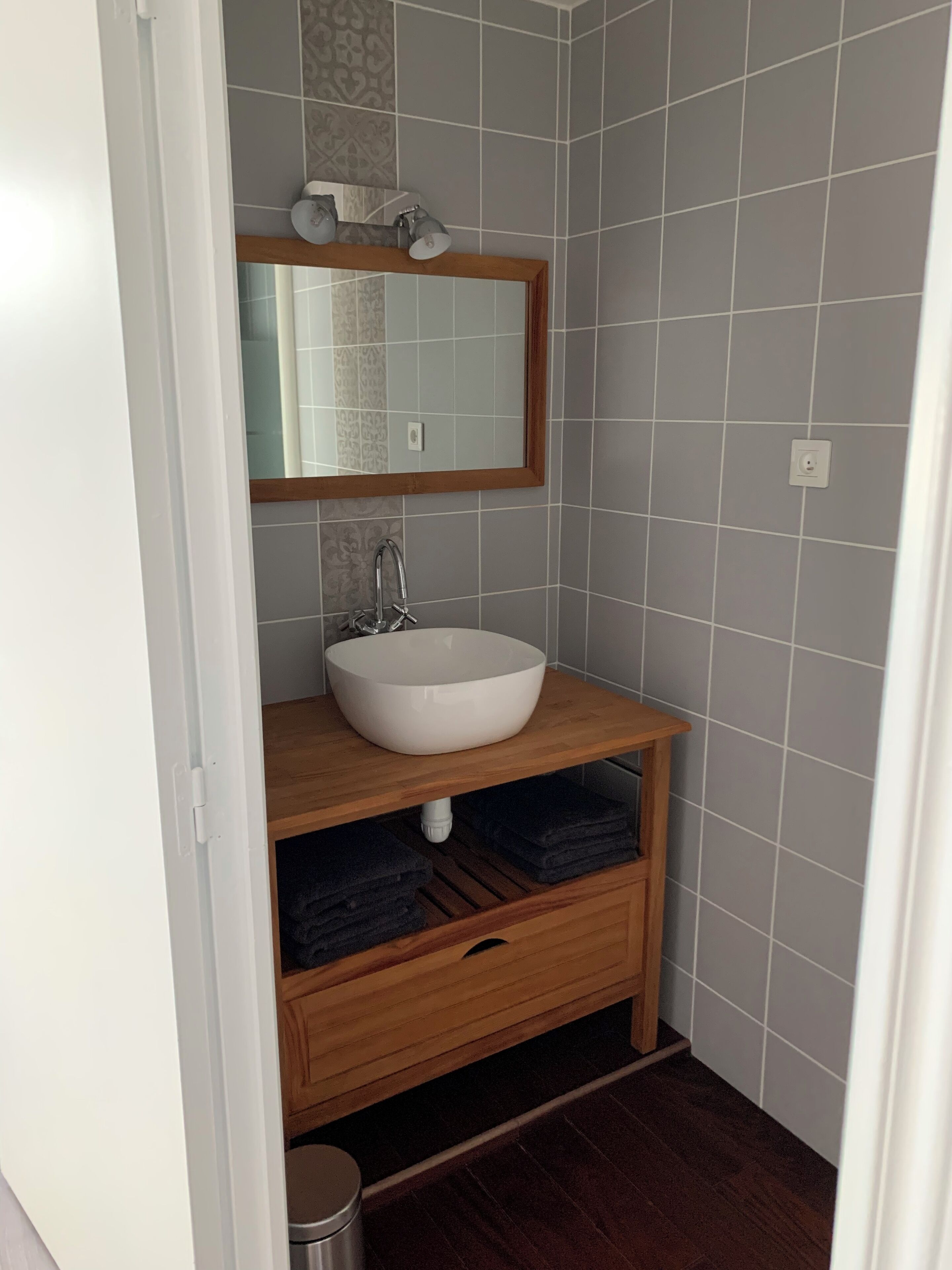 A bathroom with a white sink, wooden vanity, and a mirror.