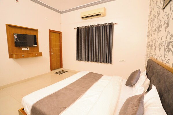 Una habitación de hotel con cama, televisor montado en la pared, aire acondicionado y una puerta.