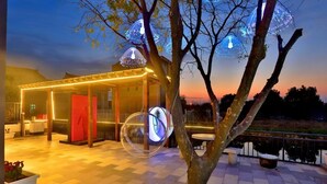 Un espacio al aire libre con un edificio moderno, un árbol y luces decorativas.