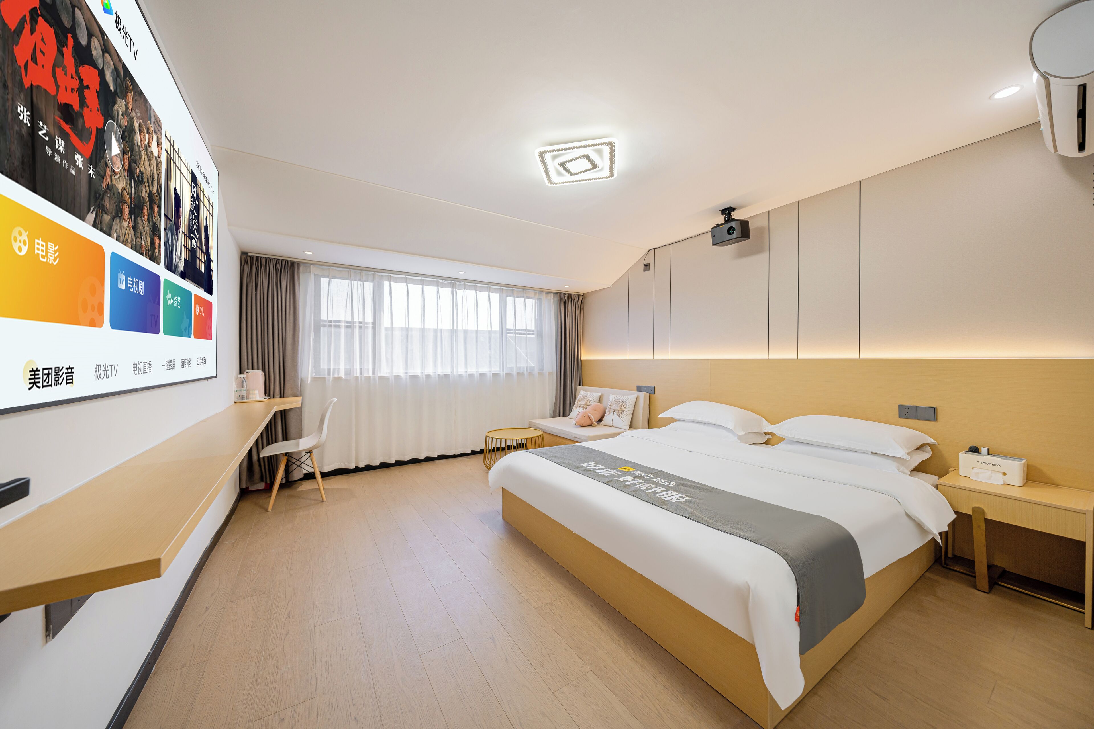 A hotel room with a large bed, a desk, and a chair. There is a window with curtains and a ceiling light.