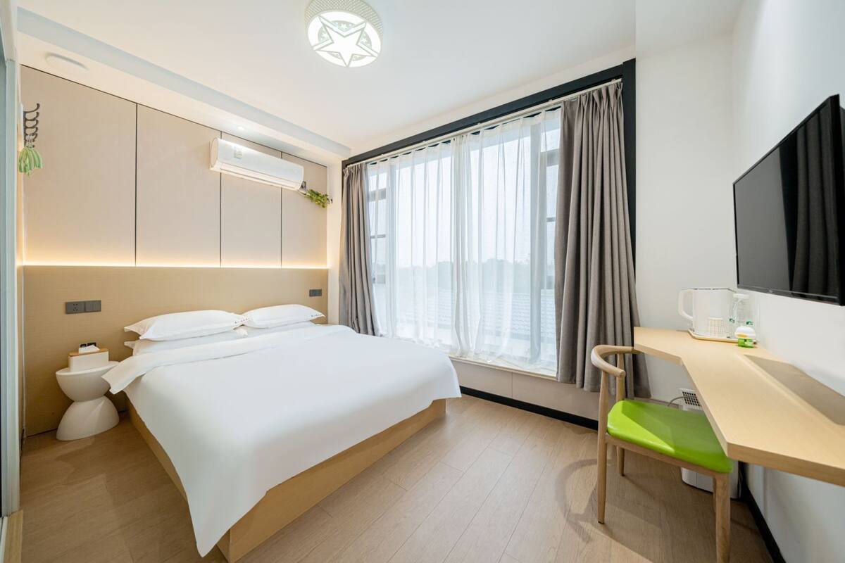 Quarto de hotel com cama, escrivaninha, cadeira, televisão e janela com cortinas.
