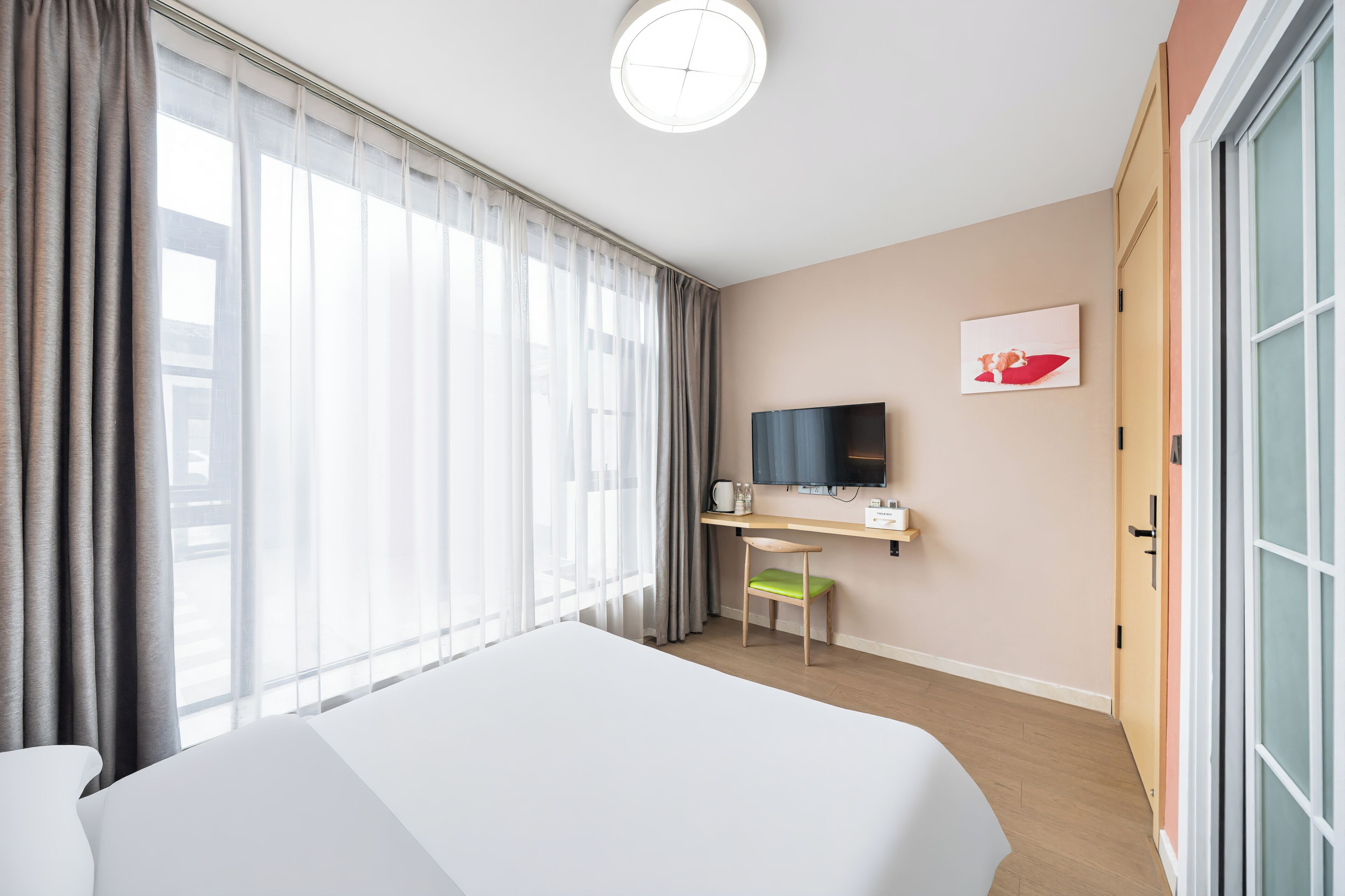 A hotel room with a bed, a desk with a chair, a television, and a window with curtains.