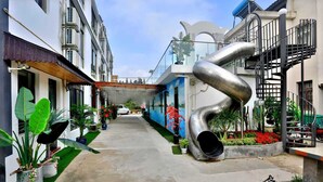 Un callejón estrecho flanqueado por edificios, una gran escultura metálica y plantas en macetas.