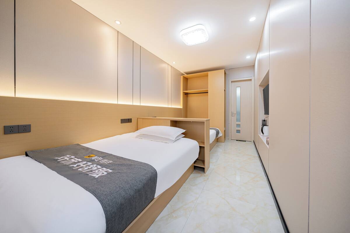Quarto de hotel moderno com cama, mesa de cabeceira e armário embutido.