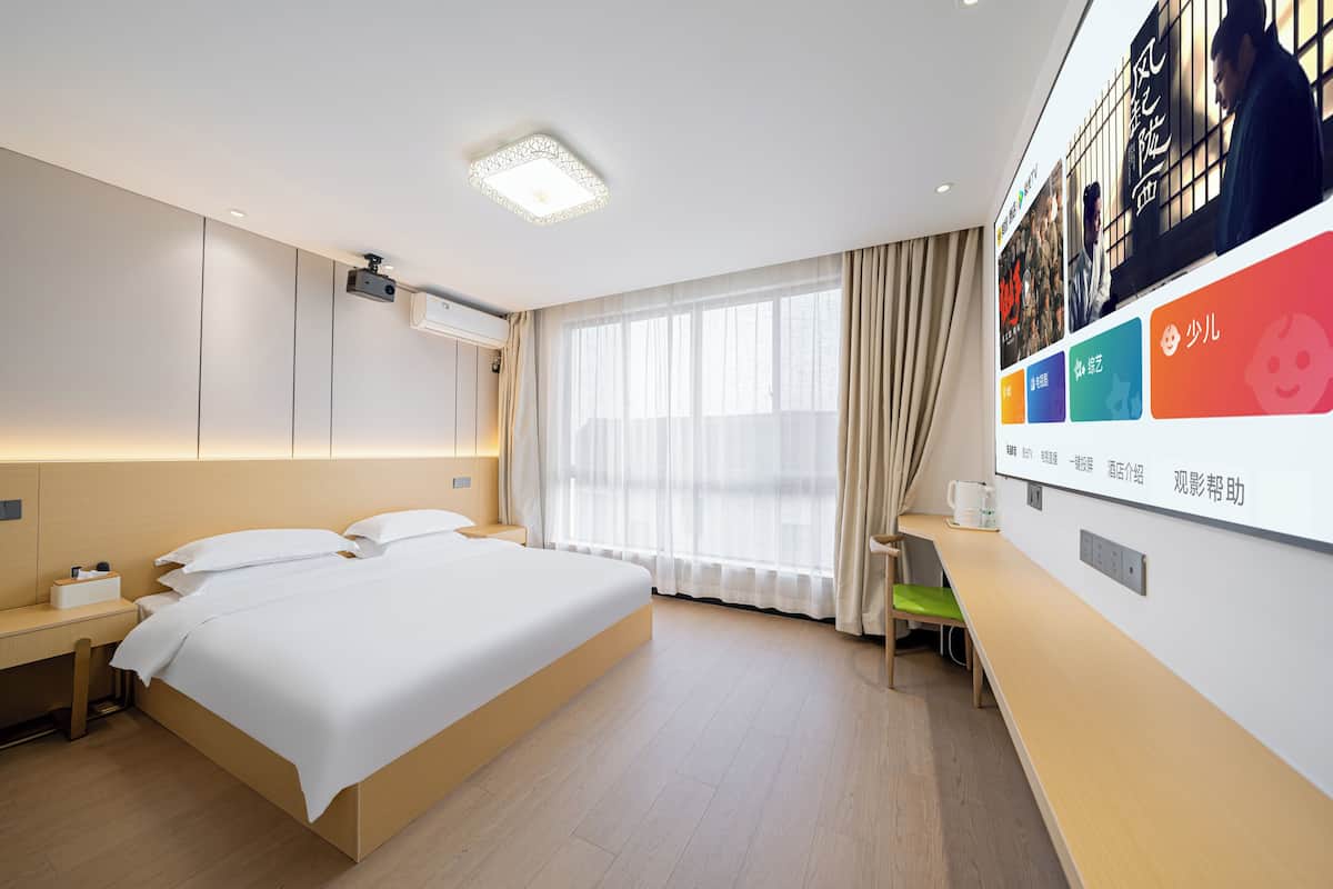 Quarto de hotel com uma cama grande, uma escrivaninha, uma cadeira e televisão na parede.