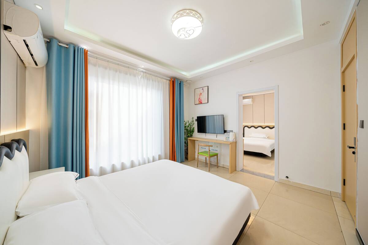Quarto de hotel com cama, escrivaninha, televisão e banheiro visível por uma porta aberta.