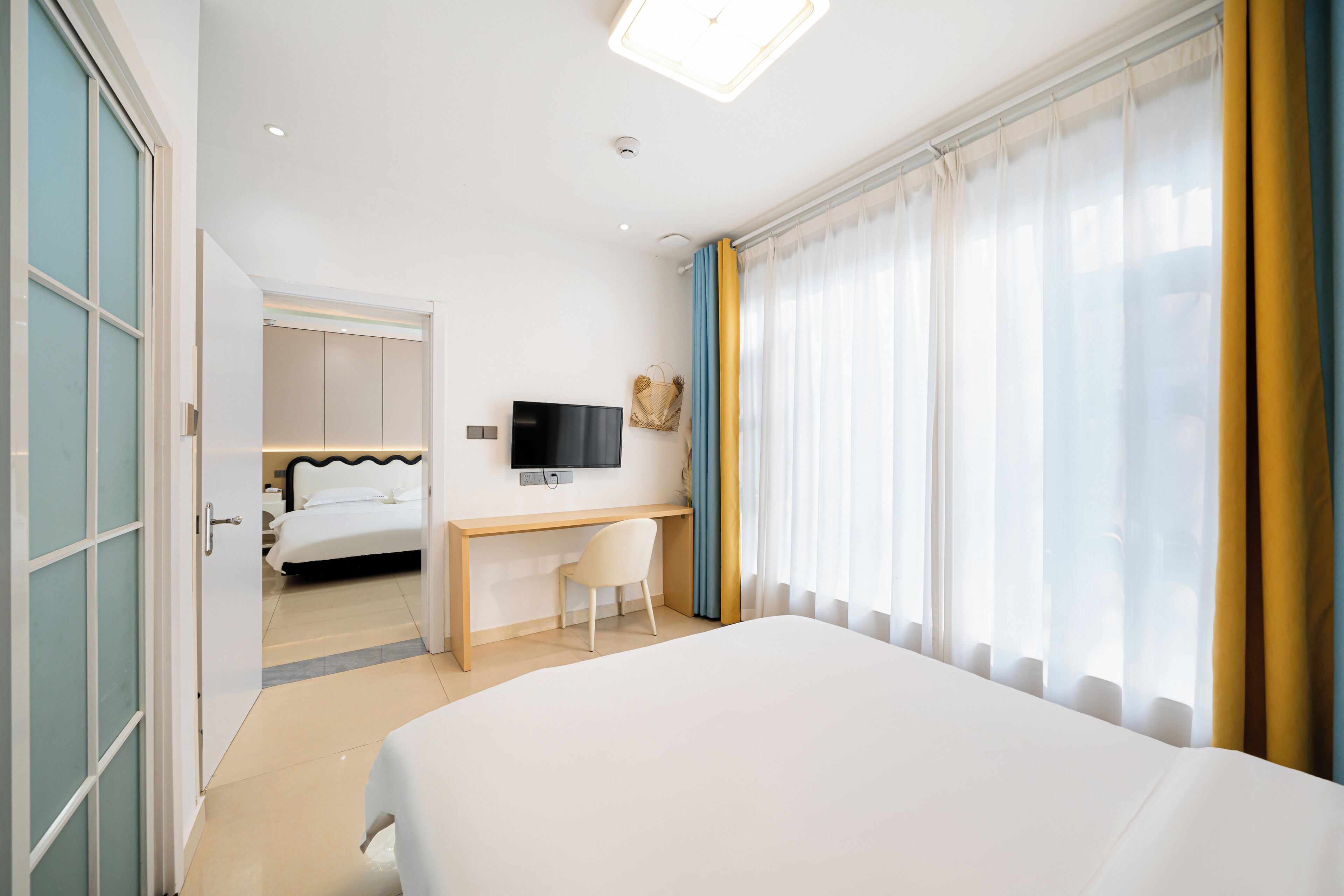 A hotel room with a bed, a desk, a TV, and a window with curtains.