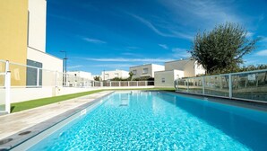 A rectangular swimming pool with clear blue water, surrounded by a white fence and a grassy area.