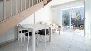 A modern interior with a wooden staircase, a dining area with white chairs, a sofa, and a view of an outdoor patio.