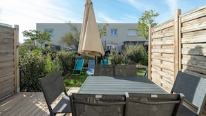 An outdoor patio with a wooden table and chairs, surrounded by a wooden fence, and a large umbrella providing shade.
