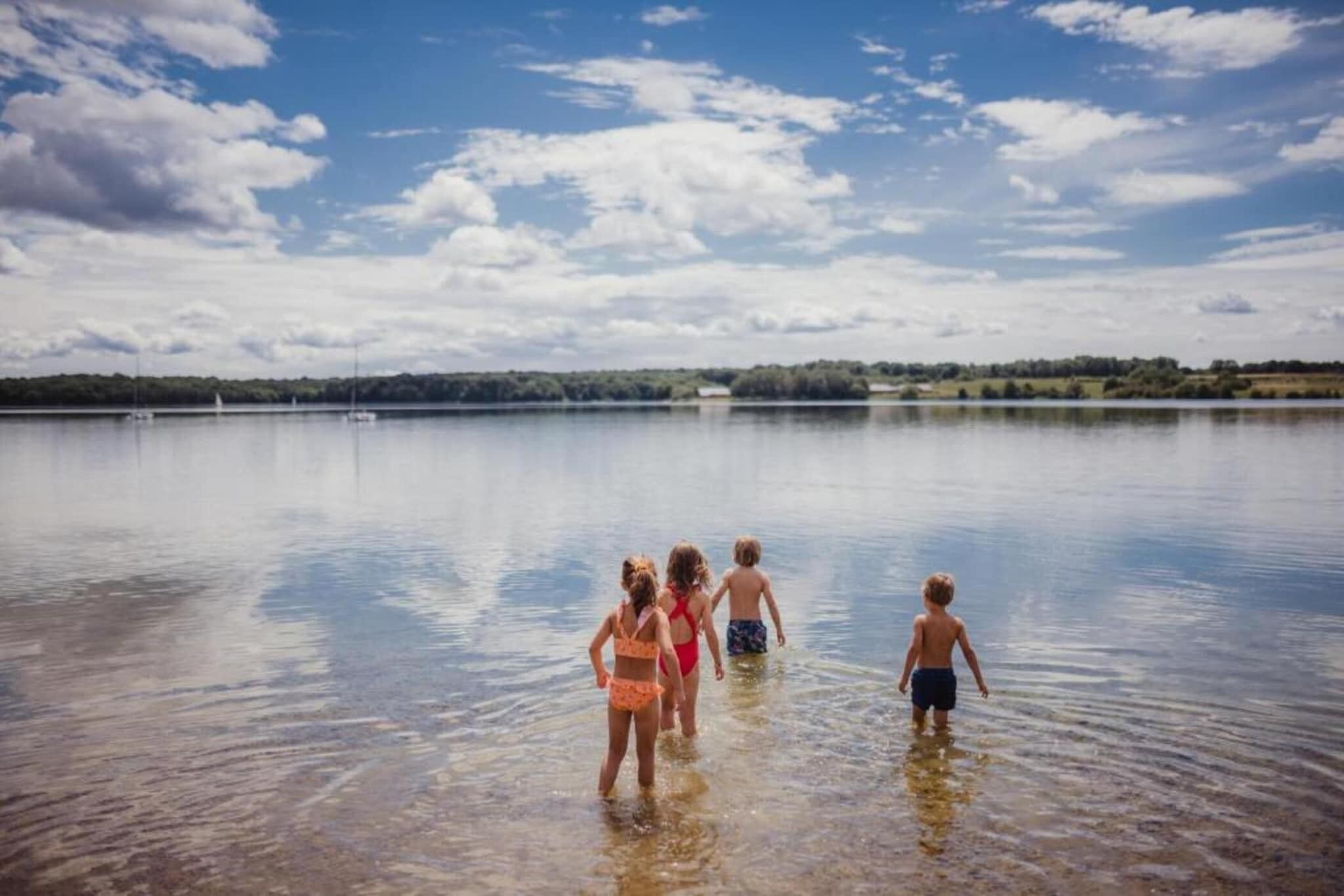 Un grupo de niños caminando en aguas poco profundas de un lago, con cielo despejado.