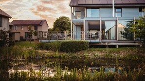 A modern two-story house with a large glass balcony, a pond in the foreground, and a cloudy sky. - Lakeside Stay with Sauna (Boussu-lez-Walcourt)