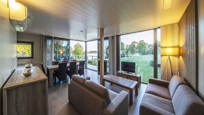 A modern living room with a sofa, coffee table, and dining area with chairs and a TV. - Lakeside Stay with Sauna (Boussu-lez-Walcourt)