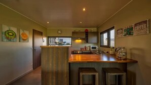 Une cuisine moderne avec des meubles en bois, un îlot central et un four à micro-ondes. On y trouve deux tabourets et un panneau décoratif sur le mur, sur le thème du café.