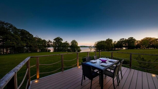 A deck with a table and chairs overlooking a body of water at dusk. - Family Villa by the Lake (Boussu-lez-Walcourt)