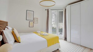 A hotel room with a bed, a yellow throw blanket, a white headboard, and a view of the outside through a sliding door. - Modern apartment - 2BDR/6P - Paris 14e (Paris)