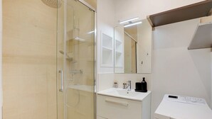A modern bathroom with a glass shower enclosure, a white sink with a mirror, and a built-in washing machine. - Modern apartment - 2BDR/6P - Paris 14e (Paris)
