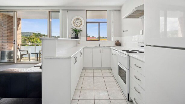 Een moderne keuken met witte kasten, een ingebouwde oven en een groot raam met uitzicht op de omgeving.