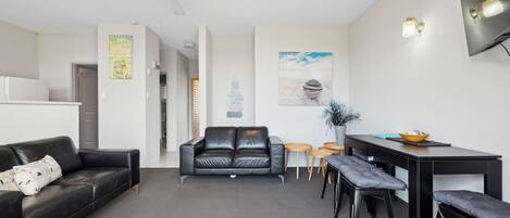 Una sala de estar moderna con un sofá y un sillón de cuero negro, y un comedor con una mesa negra y taburetes de madera.