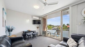 Een moderne woonkamer met een zwarte leren bank, een eethoek met een tafel en stoelen, en een balkon met uitzicht.