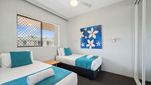 Een hotelkamer met twee bedden, een raam met uitzicht, een plafondventilator en een schilderij aan de muur.