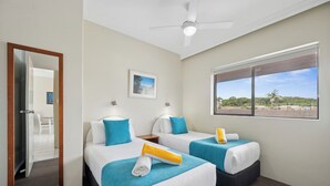 Ein Hotelzimmer mit zwei Betten, einem Deckenventilator, einem Fenster mit Blick und einer Tür zu einem Balkon.