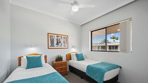 A hotel room with two beds, a ceiling fan, a window with a view, and a framed picture on the wall.
