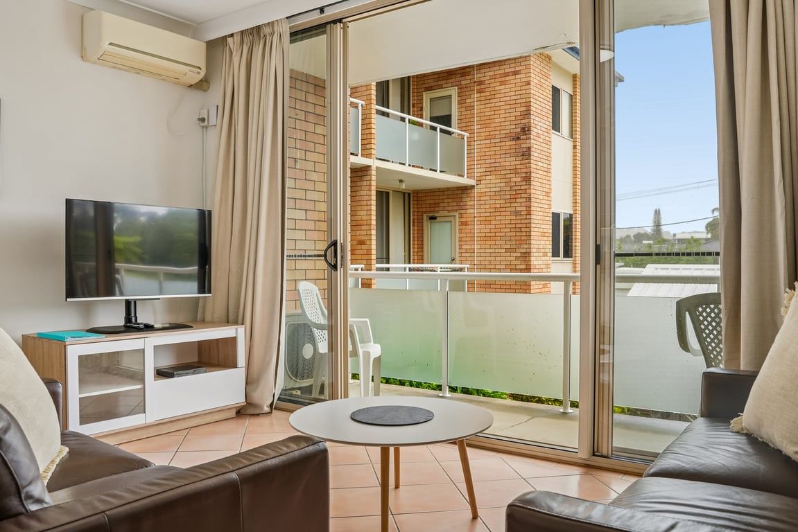 A living room with a TV, sofa, and a balcony with a table.