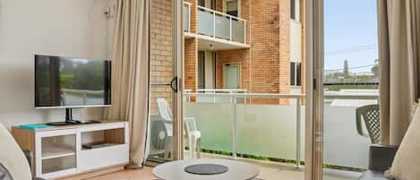 A living room with a TV, sofa, and a balcony with a table.