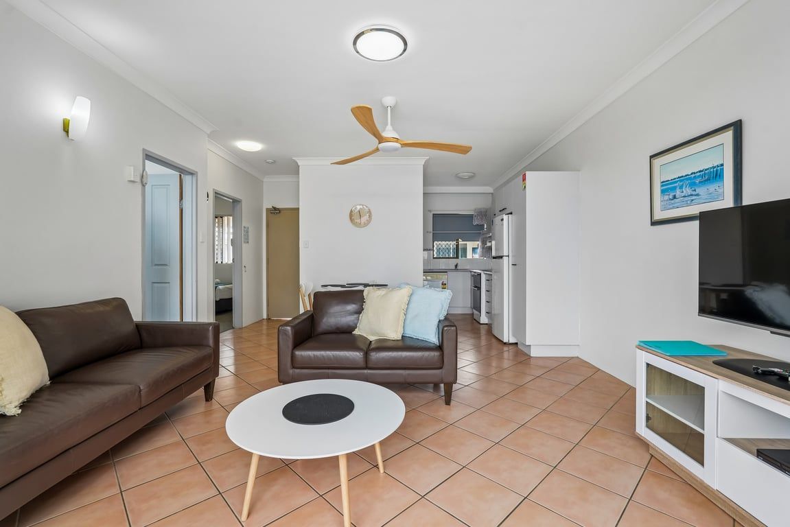 Ein Wohnzimmer mit einem braunen Ledersofa, einem weißen Couchtisch, einem Deckenventilator und einem Fernseher auf einem weißen Schrank.