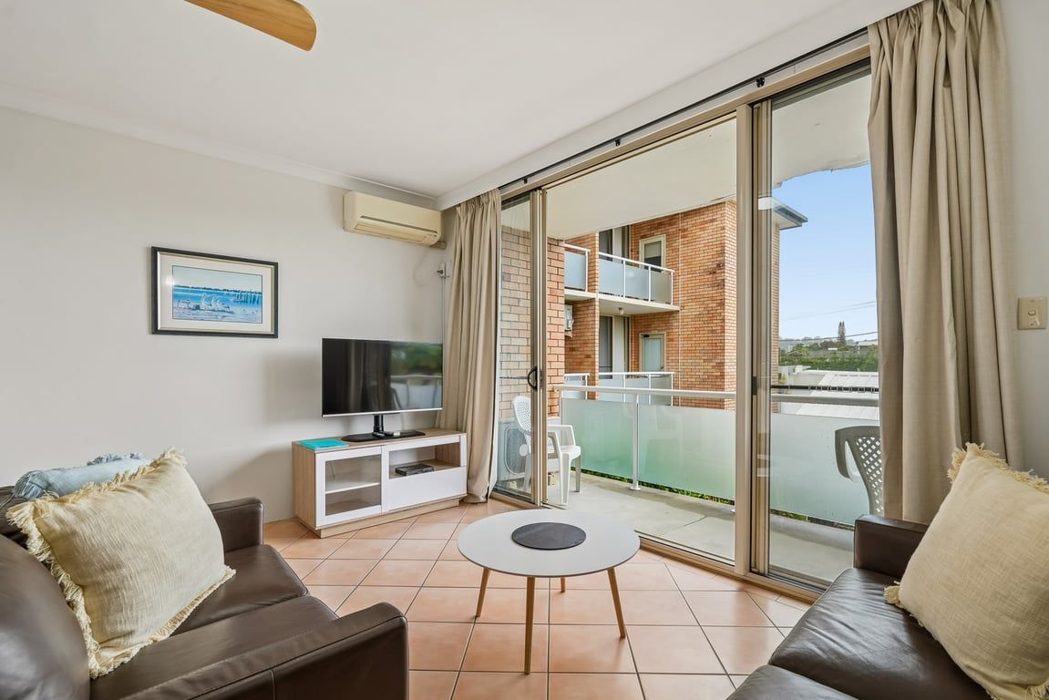 A modern living room with a sofa, a TV, a small table, and a balcony with a glass door.