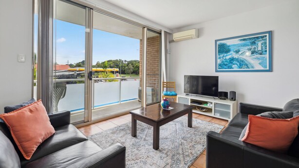 Een moderne woonkamer met een grote schuifpui naar een balkon, een flatscreen televisie en een schilderij aan de muur.