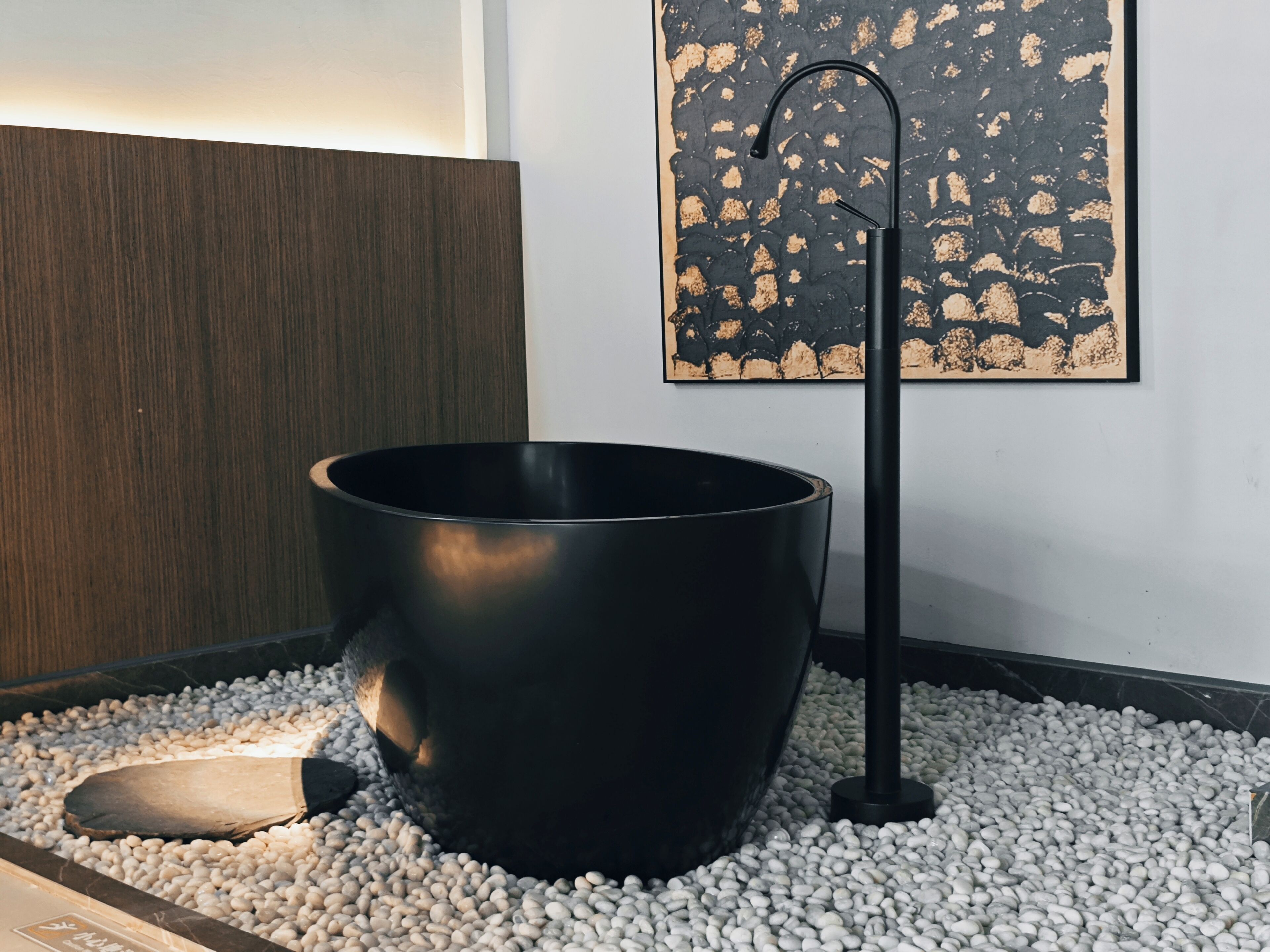 Une salle de bain moderne avec une grande baignoire noire, un mur recouvert de panneaux en bois et un tableau abstrait noir.
