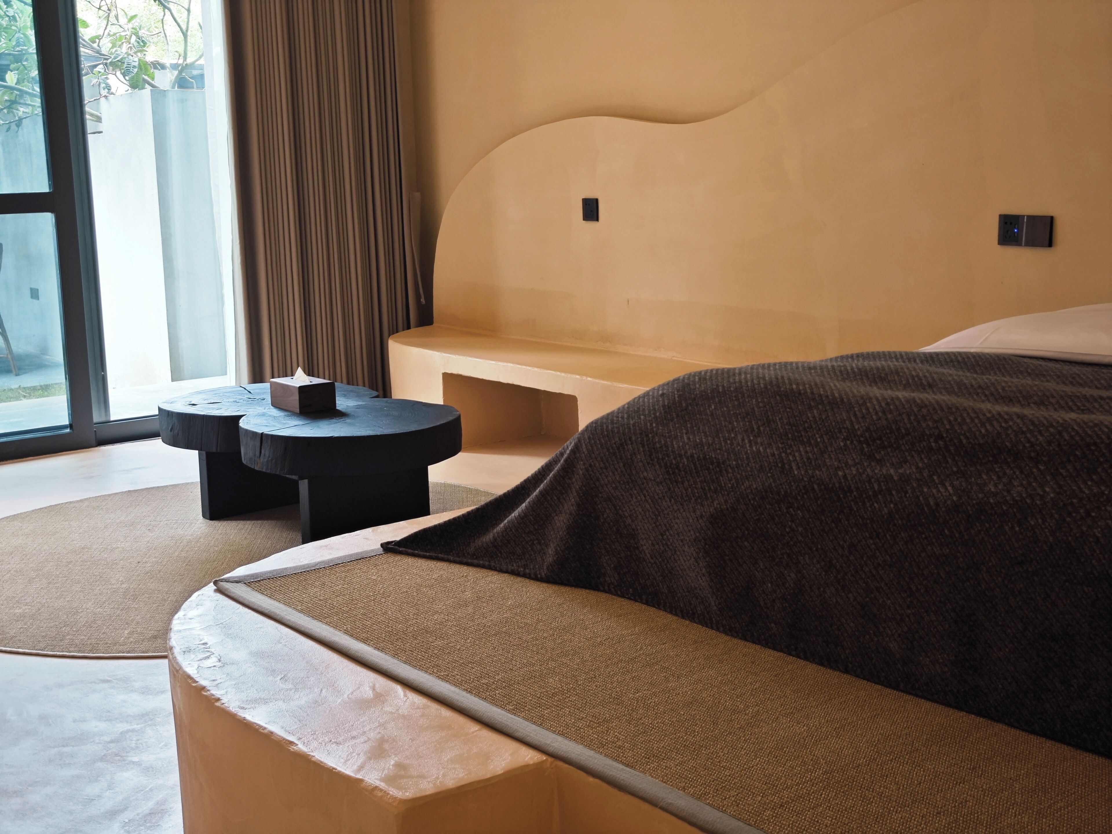 A modern hotel room with a curved bed, a small round table, and a bench.