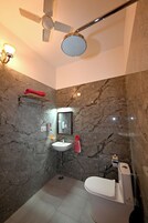 Un baño con pared de mármol, ventilador de techo, espejo redondo, lavamanos blanco y un inodoro.