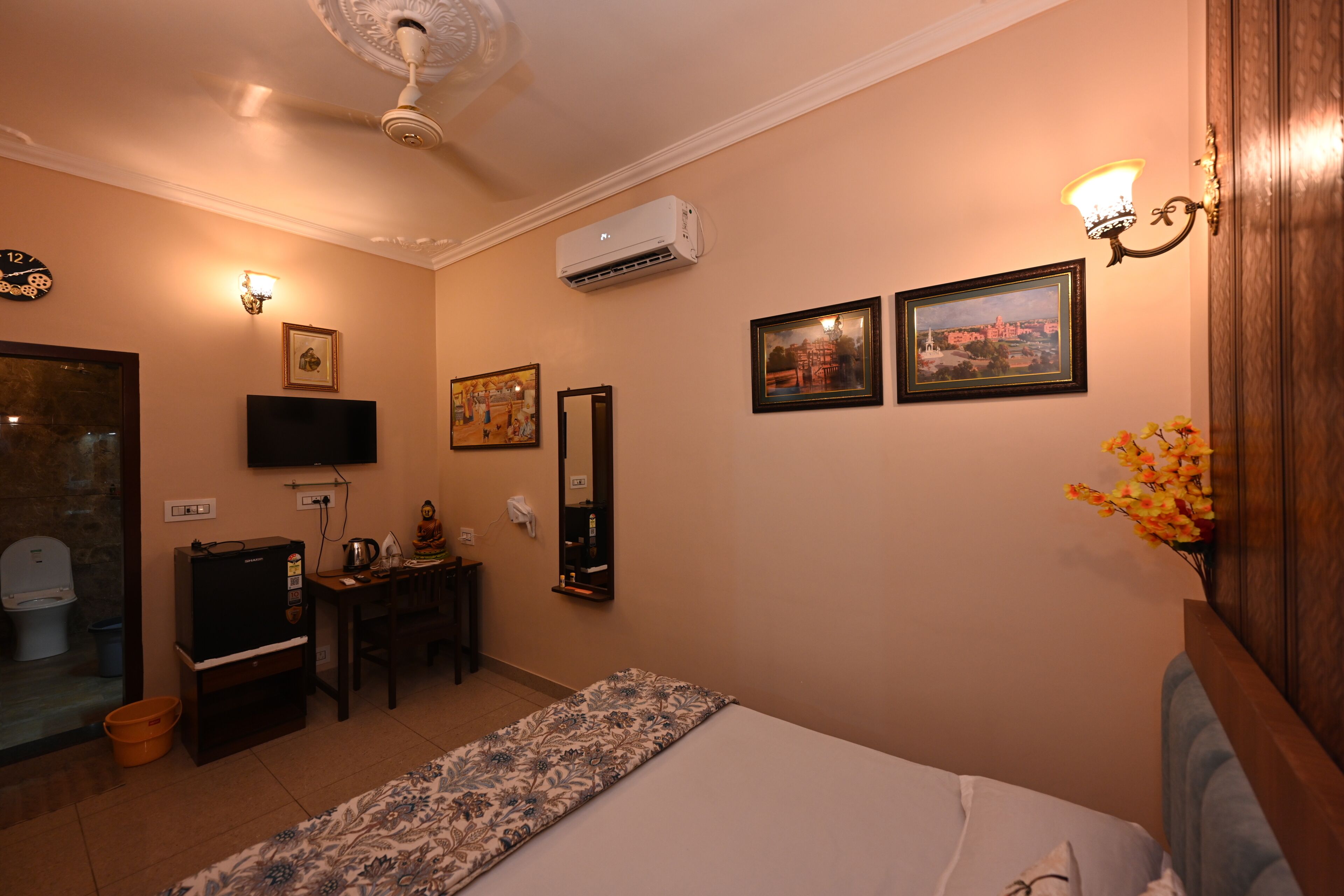 Habitación de hotel con cama, escritorio, televisión, aire acondicionado, reloj y cuadros en la pared.