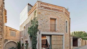 A stone building with a large sliding door, a small balcony, and a courtyard with outdoor seating.