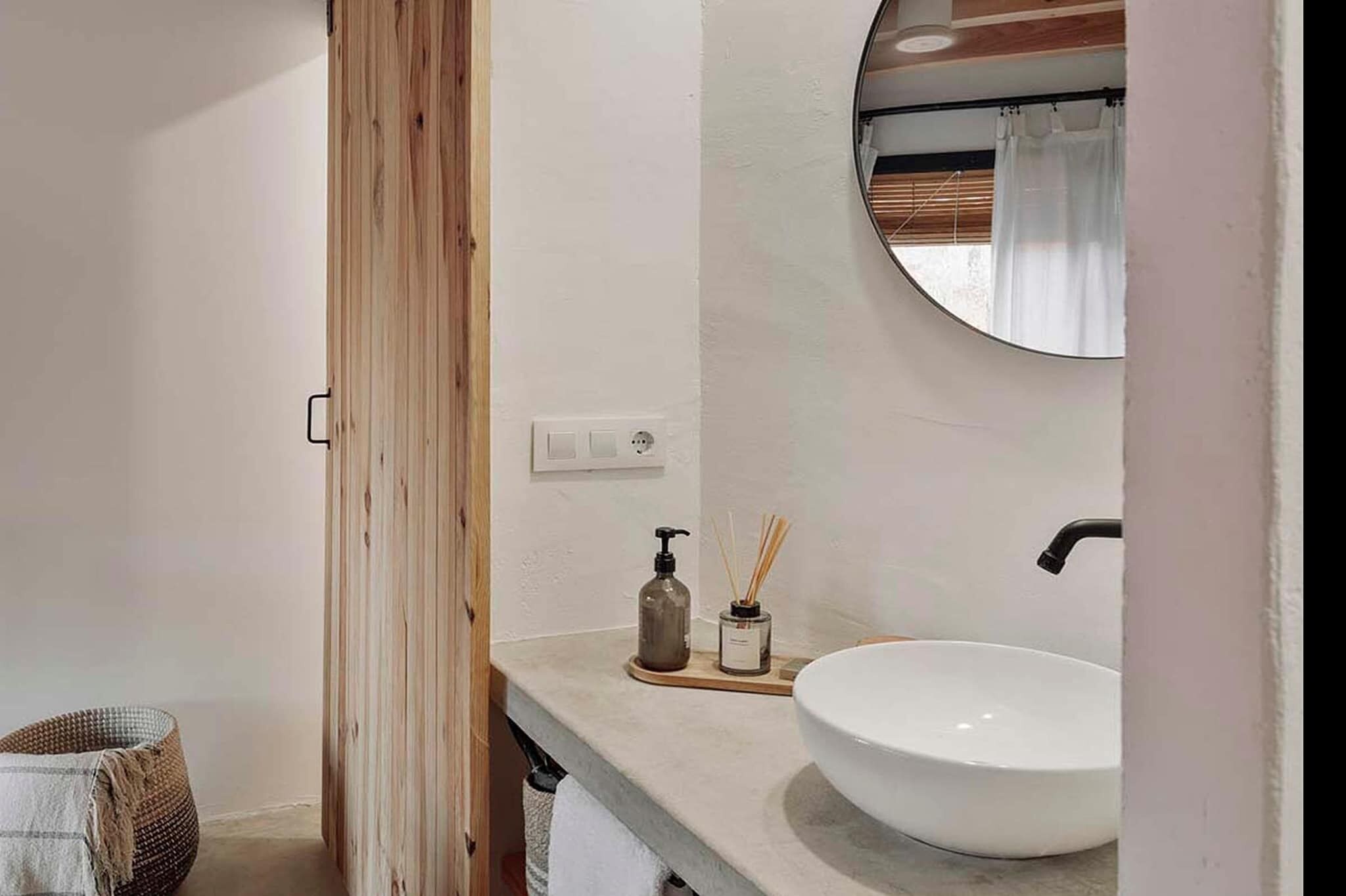 A modern bathroom with a large white sink, a round mirror, and a wooden door.