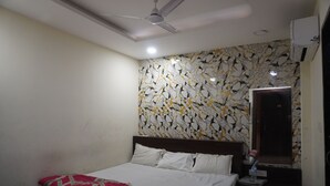 Una habitación de hotel con cama, mesita de noche, ventilador de techo y pared con diseño geométrico.