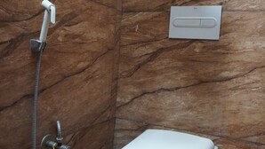Un baño con pared de mármol, inodoro blanco y cabina de ducha.