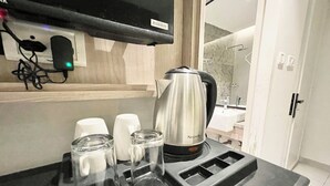 Een keukenhoek met een roestvrijstalen waterkoker, drie glazen drinkbekers en een zwart aanrecht.